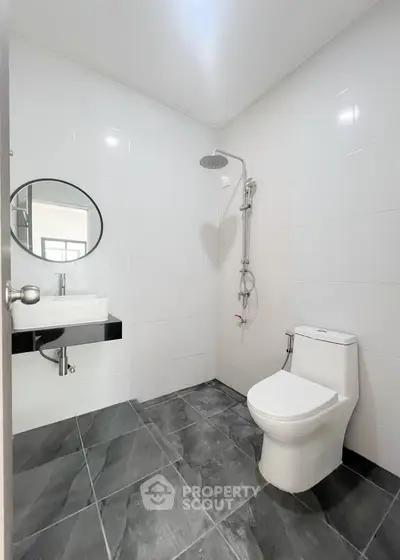 Modern bathroom with sleek fixtures and minimalist design, featuring a round mirror and contemporary shower.