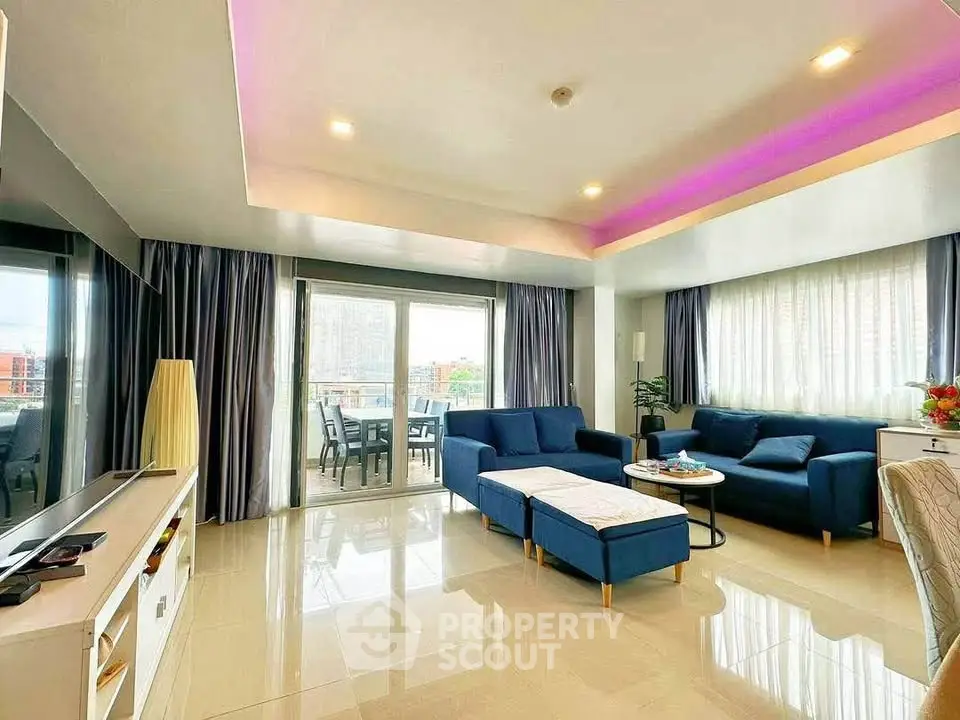 Spacious modern living room with elegant blue sofas and large windows offering natural light and city views.