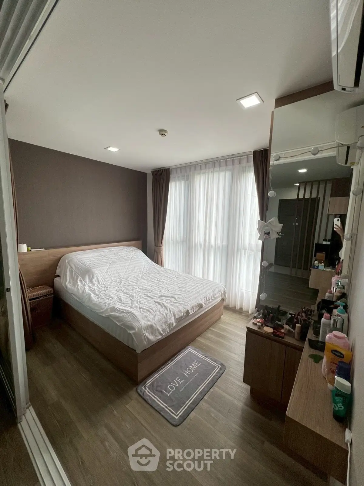 Modern bedroom with wooden flooring, cozy bed, and ample natural light from large windows.