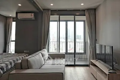 Modern living room with balcony and city view, featuring a cozy sofa and sleek TV setup.