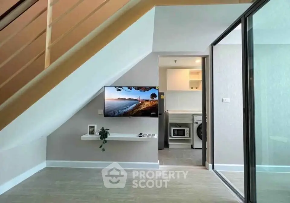 Modern duplex with sleek interior design, featuring a TV under the stairs and a compact kitchen with appliances.