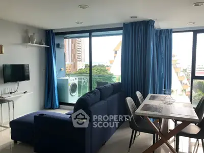 Modern living room with blue sofa and dining area, featuring large windows and balcony view.