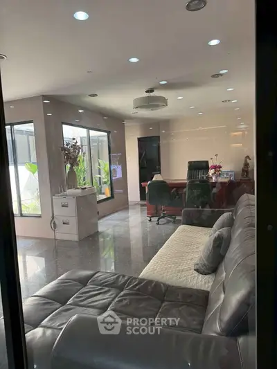 Luxurious office space with modern leather sofa and elegant desk, featuring large windows and sleek flooring.