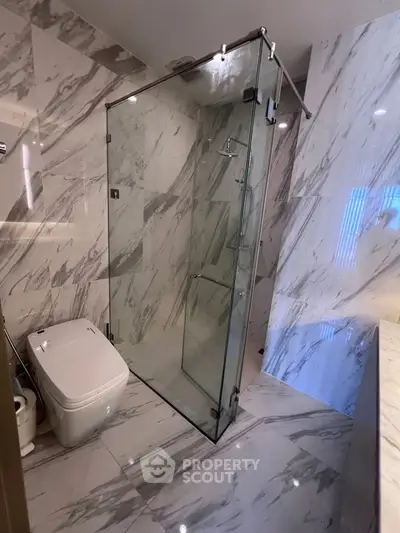 Luxurious marble bathroom with glass shower enclosure and modern fixtures.