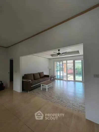Spacious living room with large windows and garden view, featuring a comfortable sofa and ceiling fan.