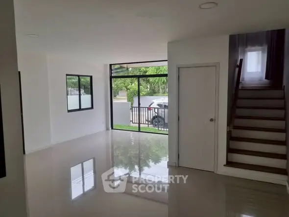 Spacious modern living room with large windows and staircase, offering natural light and sleek design.