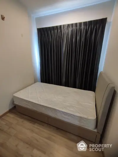 Cozy bedroom with a large window draped in elegant black curtains, featuring a comfortable bed awaiting its new owner's personal touch.