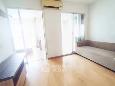 Cozy living room with wooden flooring and natural light, featuring a comfortable sofa and air conditioning.