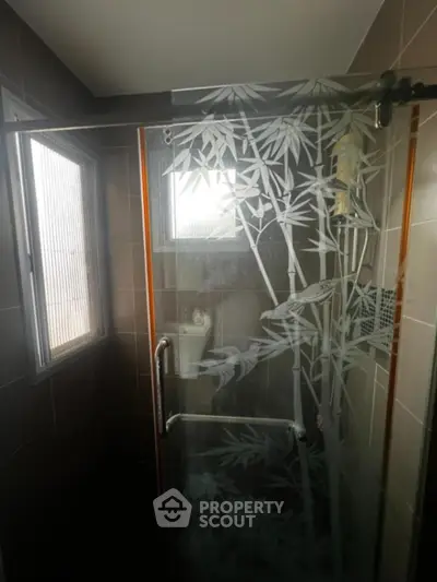 Elegant bathroom with artistically etched glass shower enclosure and natural light filtering through frosted window, enhancing the serene ambiance.