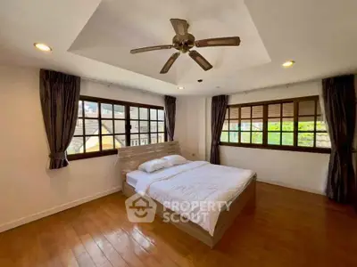 Spacious bedroom with wooden flooring and large windows offering natural light.