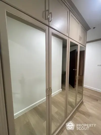 Elegant bedroom with large mirrored wardrobe doors reflecting a spacious interior, featuring high-quality wooden flooring and tasteful neutral decor.