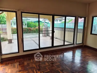 Spacious living room with large windows and wooden flooring, offering a view of the outdoor patio.