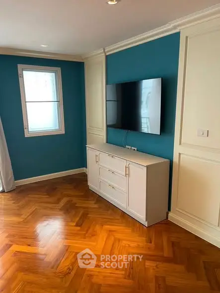 Stylish living room with elegant parquet flooring and mounted TV, featuring chic teal accent wall.