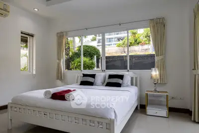 Spacious bedroom with large windows and modern decor in a serene setting.