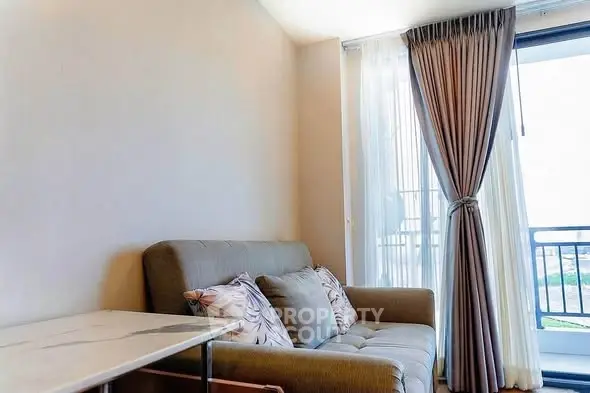 Cozy living room with plush sofa and elegant curtains opening to a balcony with a view.