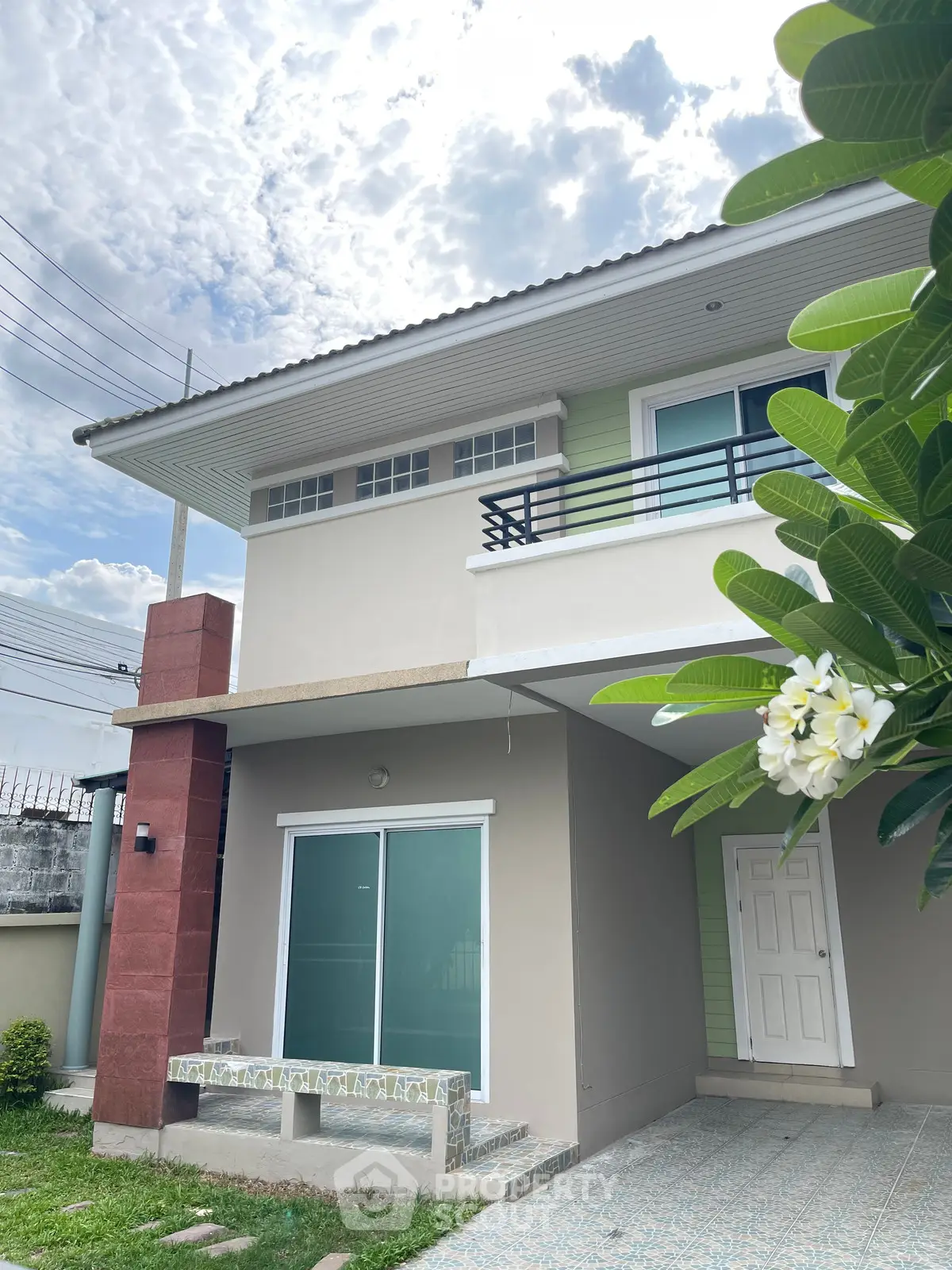 Modern two-story house with balcony and lush greenery under a bright sky.