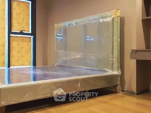 Spacious bedroom with new bed frame wrapped in protective plastic, ready for move-in.