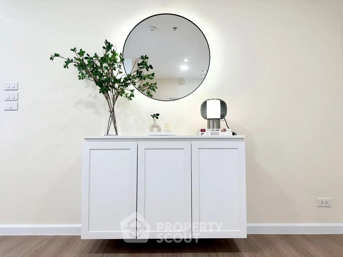 Modern minimalist interior with white cabinet, round mirror, and decorative plant.