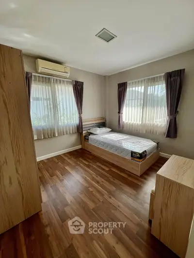 Cozy bedroom with wooden flooring and natural light from large windows.