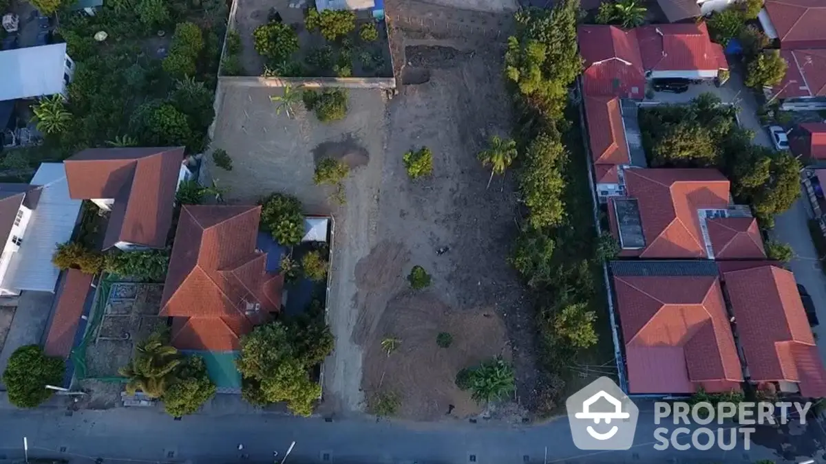 Aerial view of residential land plot surrounded by houses with red roofs and lush greenery.