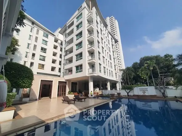 Luxurious apartment building with pool and lush greenery under clear blue sky.