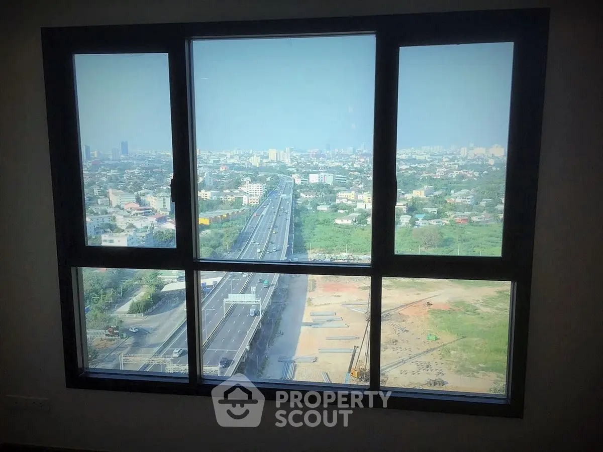 Stunning cityscape view from high-rise apartment window, showcasing urban skyline and highway.