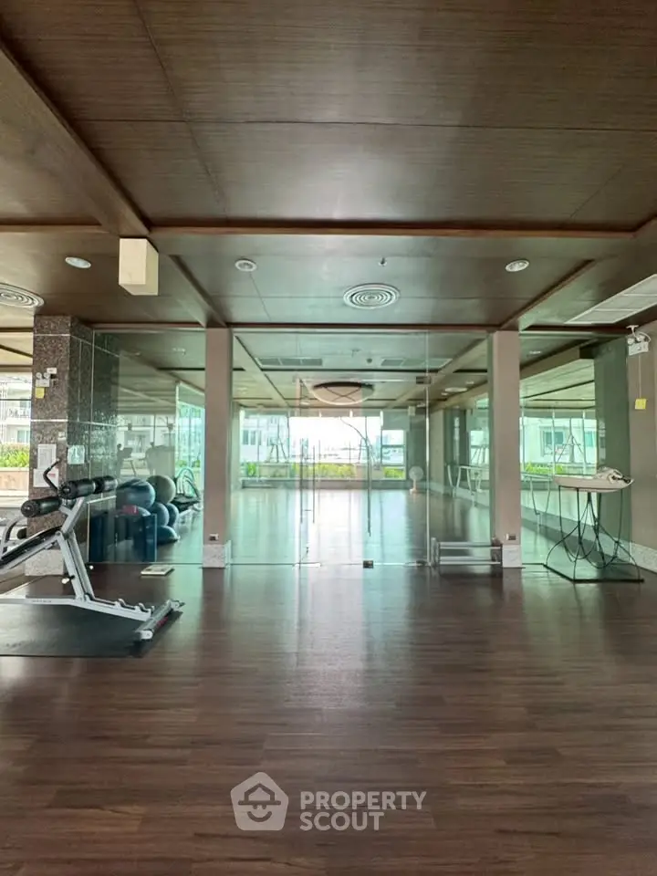 Spacious modern gym with glass walls and wooden flooring in luxury apartment complex.