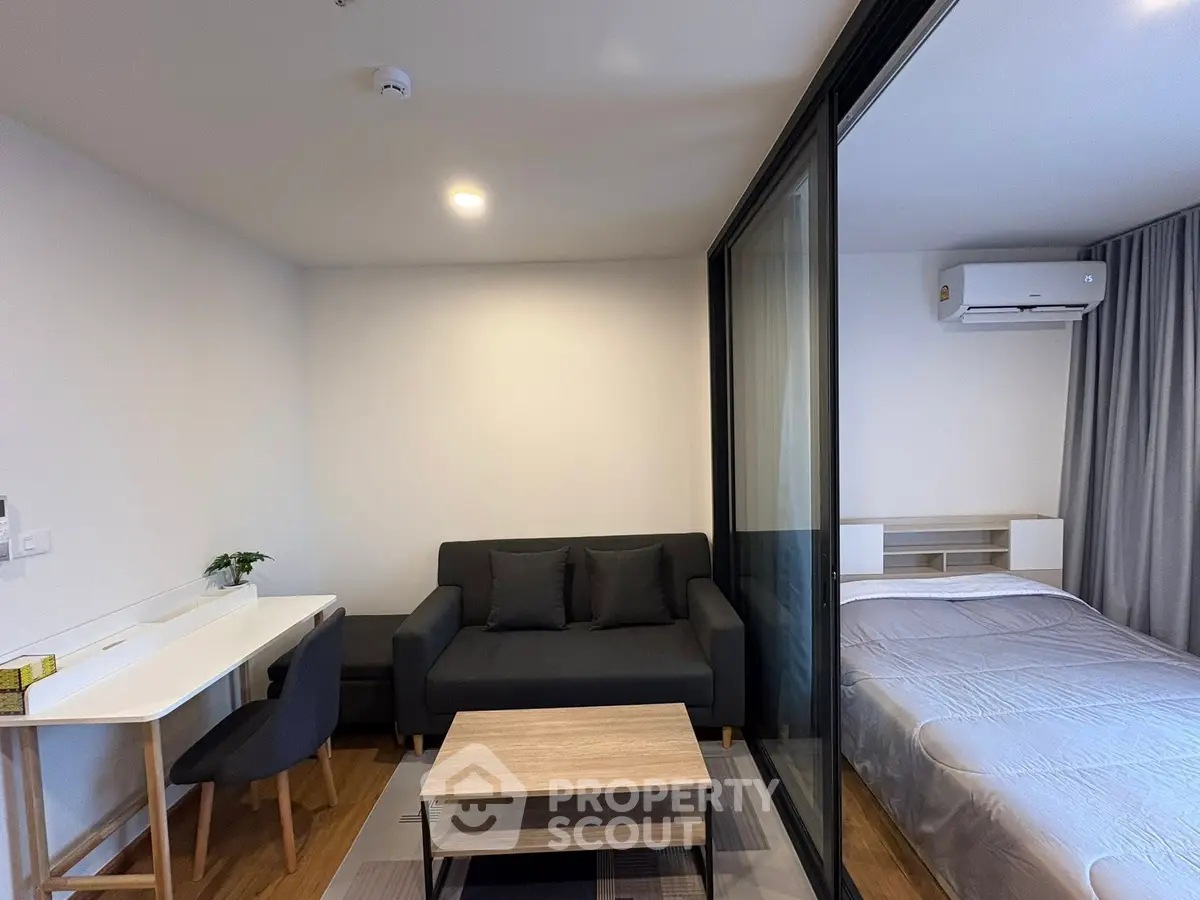 Modern studio apartment with cozy living area and bedroom separated by glass partition.