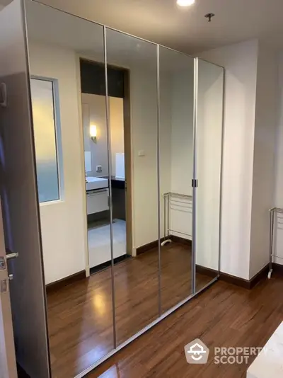 Spacious bedroom with mirrored wardrobe and wooden flooring