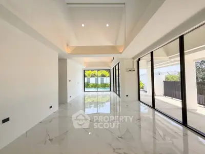 Spacious modern living room with marble floors and large windows overlooking a pool and garden.