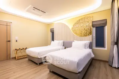 Modern bedroom with twin beds and stylish decor, featuring warm lighting and wooden flooring.