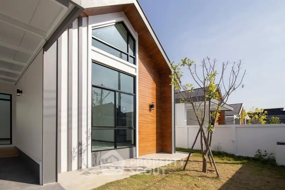 Modern house exterior with large windows and wooden accents in a sunny garden setting.