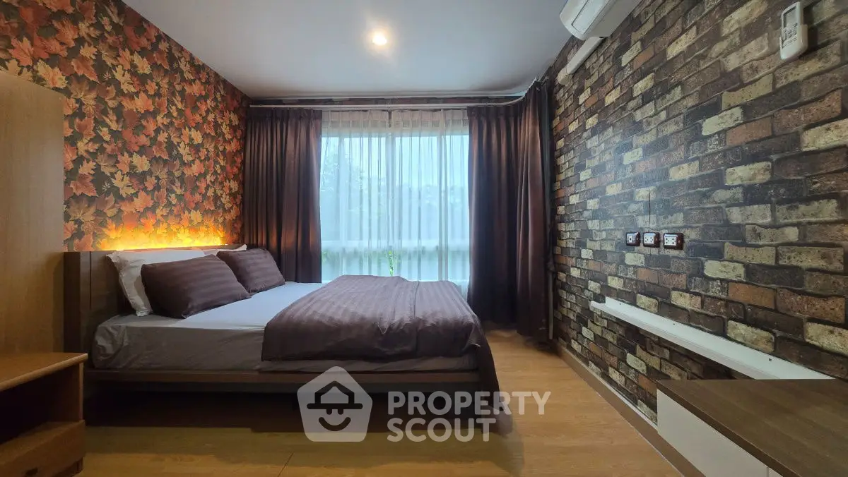 Cozy bedroom with stylish brick and leaf wallpaper, featuring a large window with curtains.