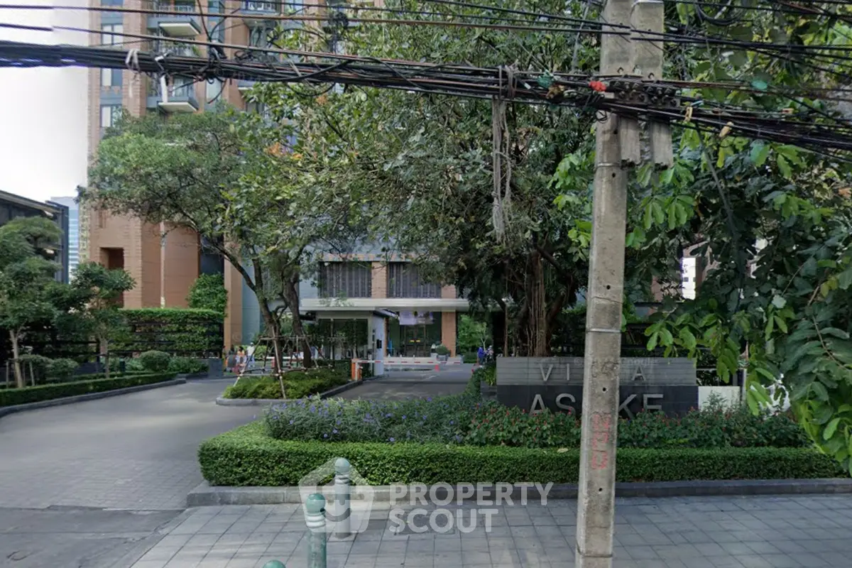 Modern residential building entrance with lush greenery and paved driveway in urban setting.