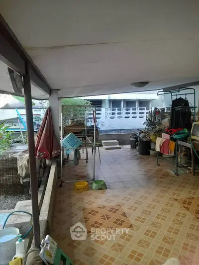 Spacious covered outdoor area with tiled flooring and various household items.