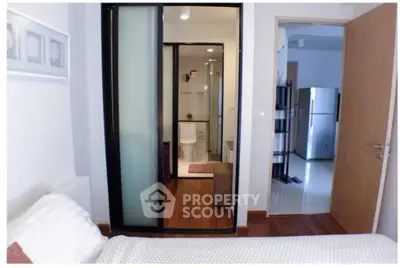 Modern bedroom with ensuite bathroom and view of kitchen area, featuring sleek design and wooden flooring.