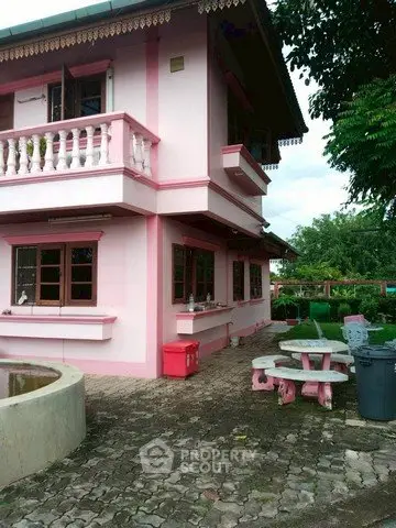 Charming pink two-story house with outdoor seating and lush greenery, perfect for family living.