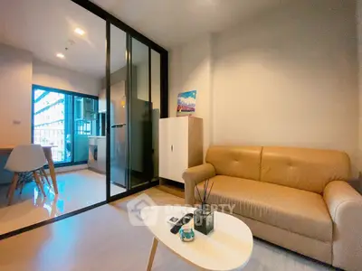 Modern living room with sleek furniture and glass partition leading to a stylish kitchen area.