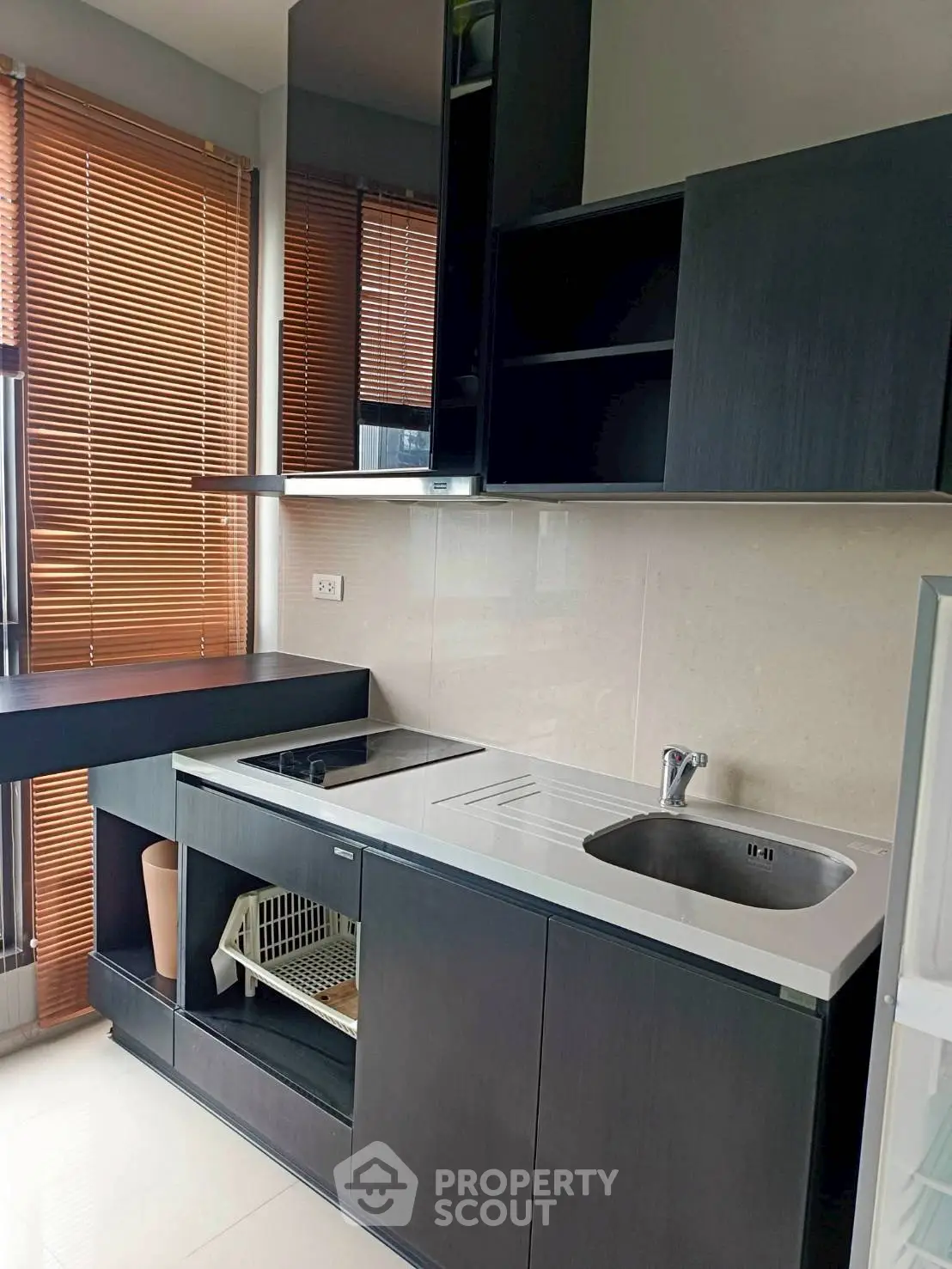 Modern kitchen with sleek black cabinets and large windows with wooden blinds.