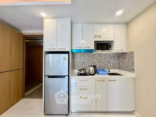 Modern kitchen with sleek cabinetry, built-in microwave, and compact fridge in a stylish apartment.