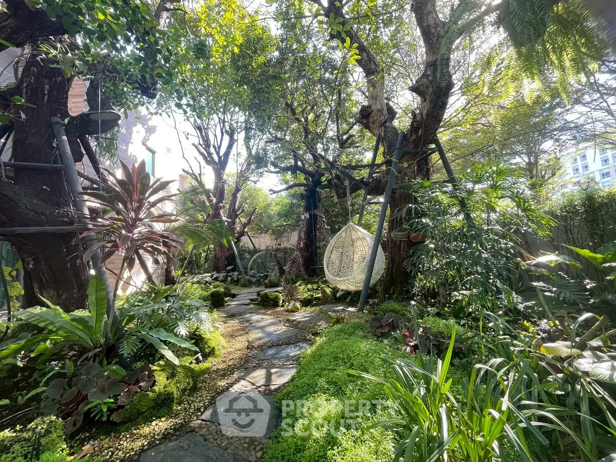 Lush garden with stone pathway and hanging chair, perfect for relaxation and outdoor enjoyment.