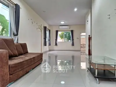 Spacious living room with modern sofa and glass coffee table, featuring large windows and elegant curtains.