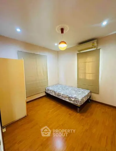 Cozy bedroom with wooden flooring and air conditioning, featuring a single bed and neutral decor.