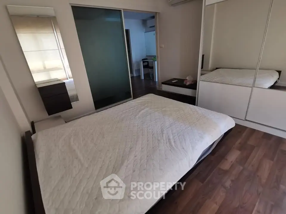 Spacious bedroom with wooden flooring and mirrored wardrobe in modern apartment.