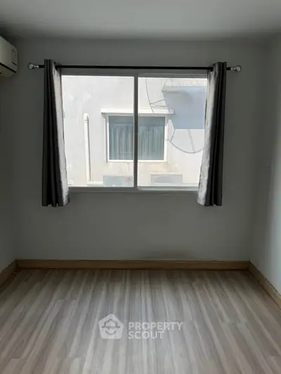 Bright empty room with large window and wooden flooring, perfect for customization.