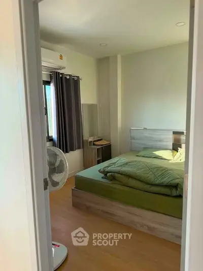 Cozy bedroom with wooden flooring and modern furnishings, featuring a large window for natural light.