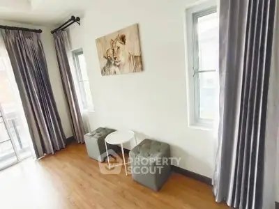 Bright living room with large windows and elegant curtains, featuring modern decor and wooden flooring.