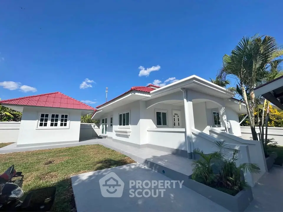 Charming white bungalow with red roof and lush garden under clear blue sky