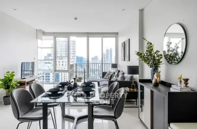 Modern living room with dining area and city view, featuring sleek furniture and large windows.