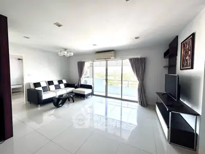 Spacious modern living room with sleek furniture and large windows leading to a balcony.
